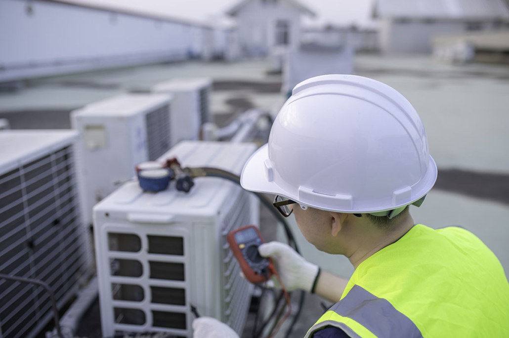 Man wearing white hard hat, safety sunglasses and checking commercial HVAC system on roof top